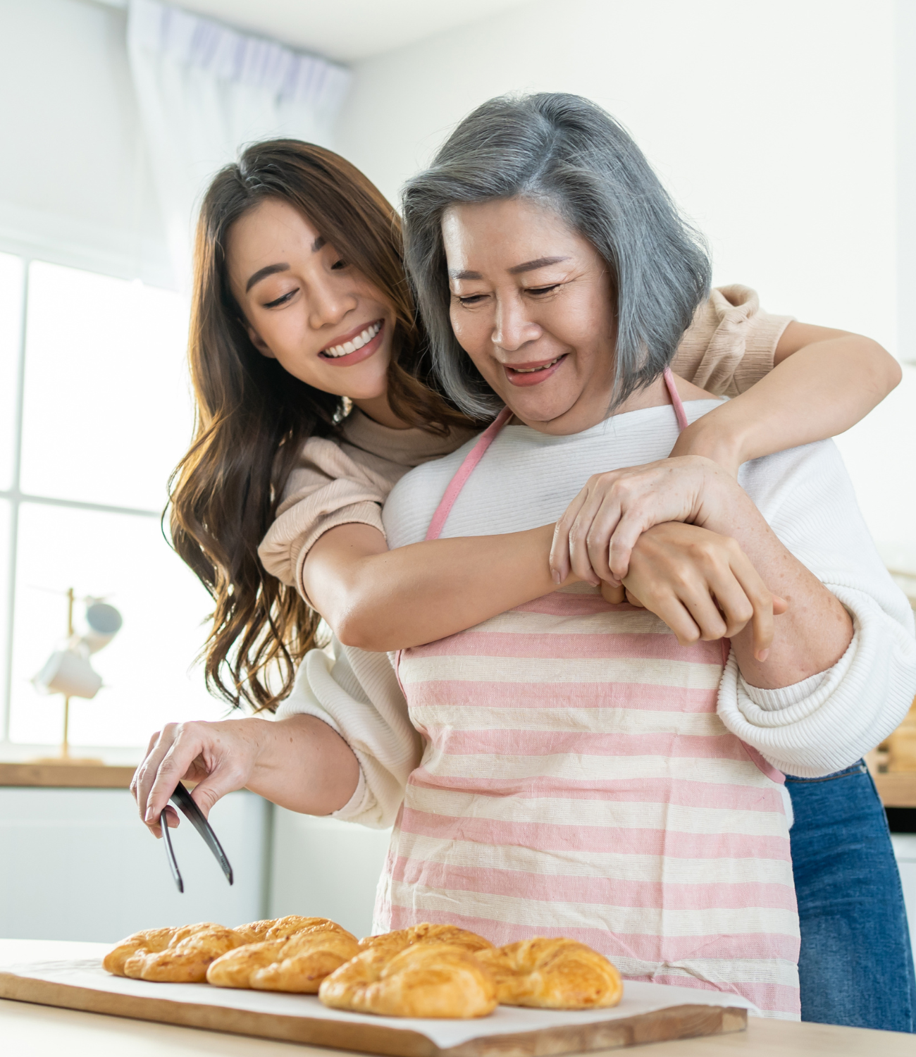 a woman embracing an older woman over the shoulders, as she is picking up food with tongs